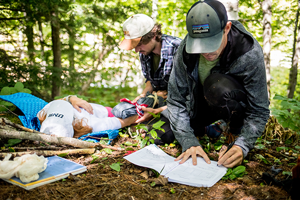 Two people administering first aid to an injured individual in a wooded area.