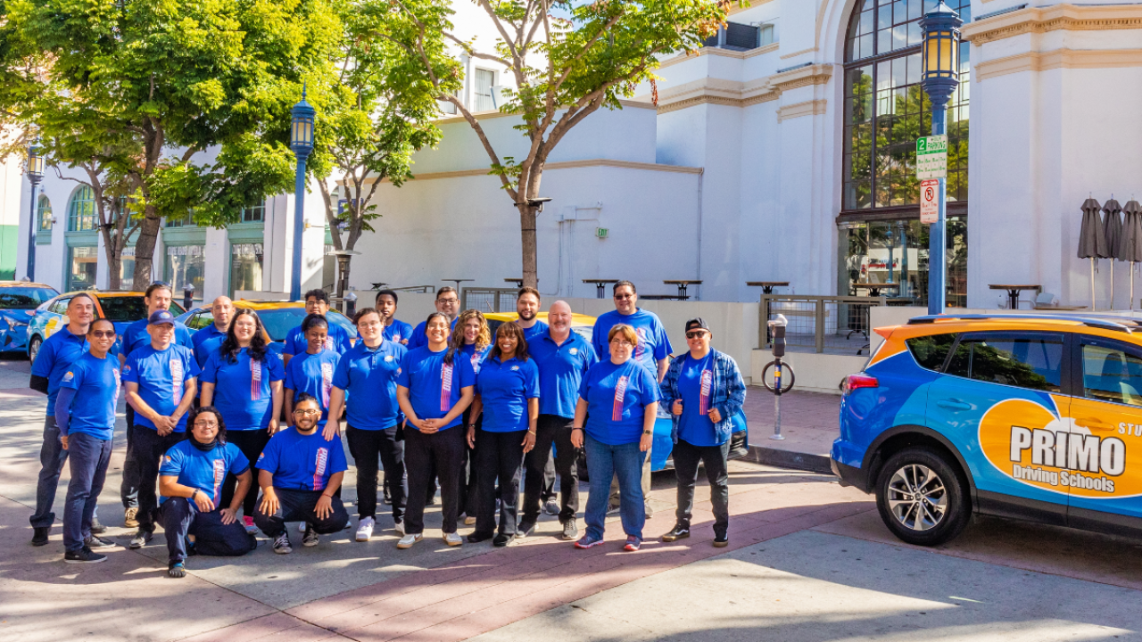 Employees of Primo Driving School, standing next to a branded car, posing as a group in Westwood Village