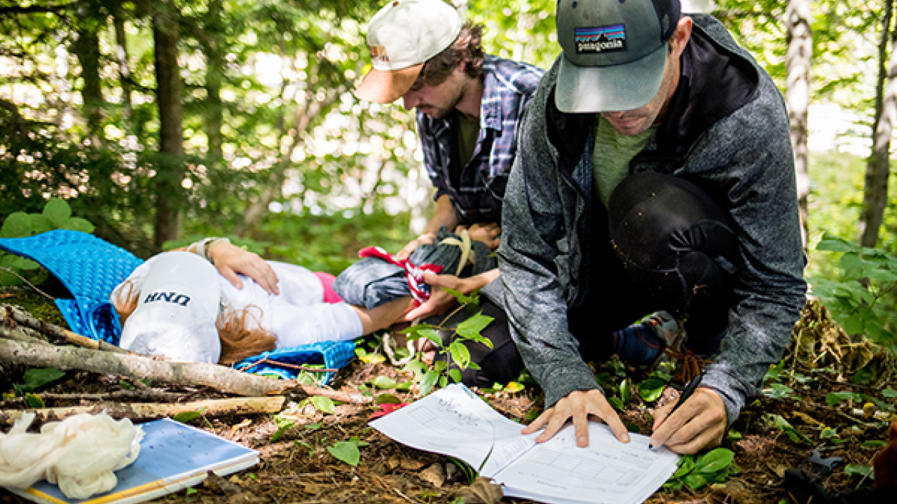 Two people administering first aid to an injured individual in a wooded area.