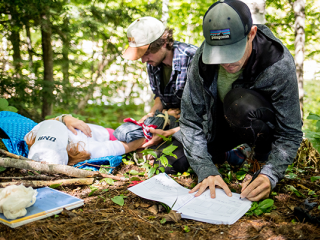 Two people administering first aid to an injured individual in a wooded area.